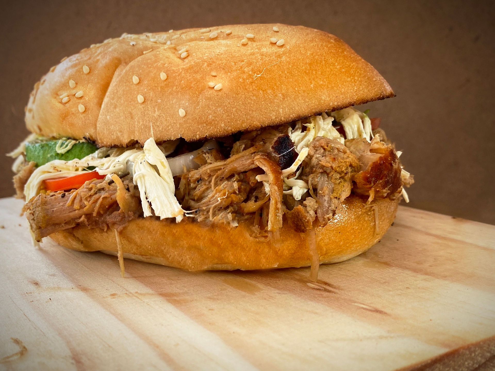 Mouth-watering close-up of a pulled pork sandwich with fresh ingredients and sesame seed bun.